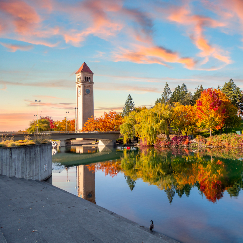 Vivid fall colors of red, orange, and yellow at the Spokane Washington Riverfront Park along the Spokane River with the Great Northern Clock Tower in view.